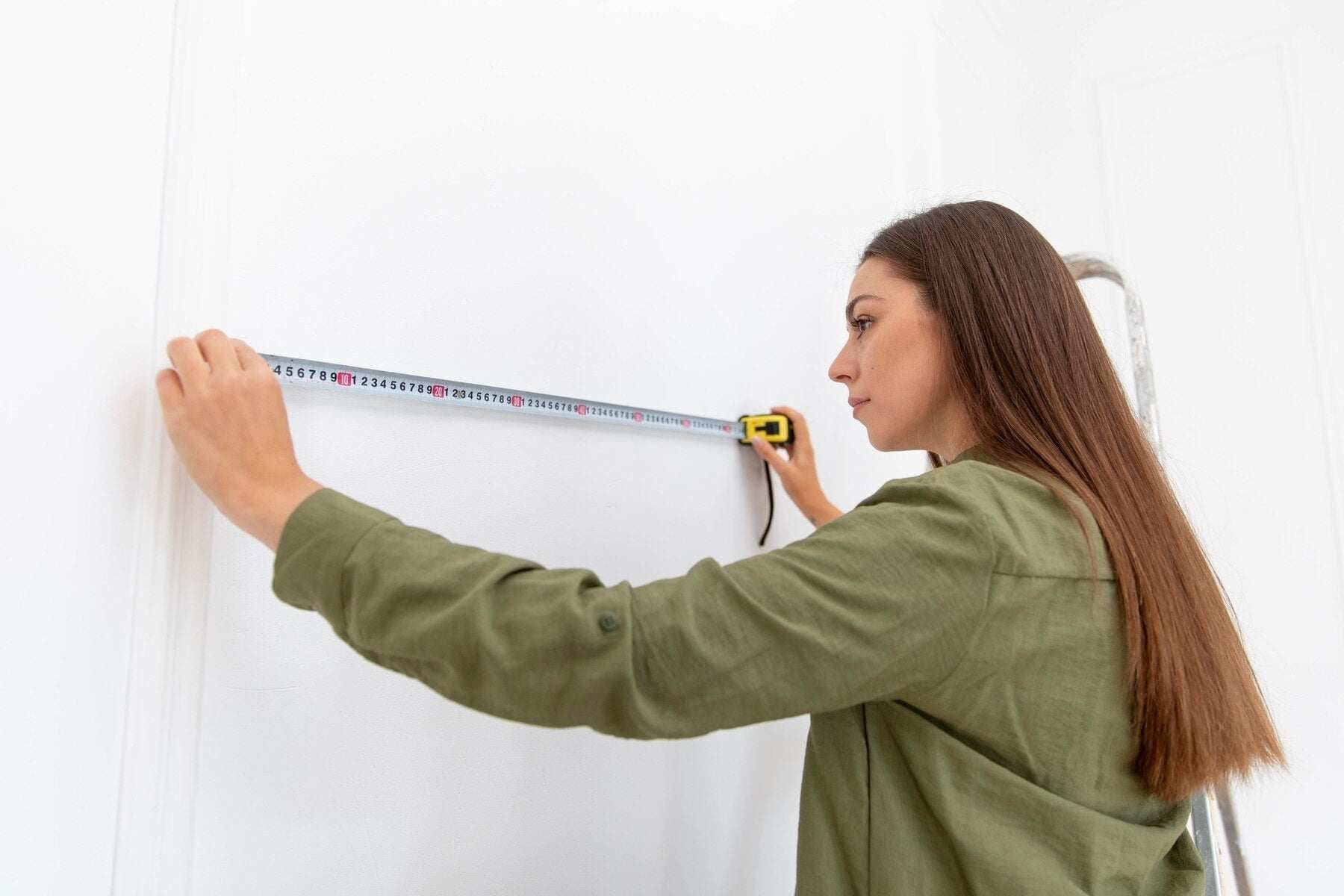 Femme mesurant un mur blanc avec un mètre ruban